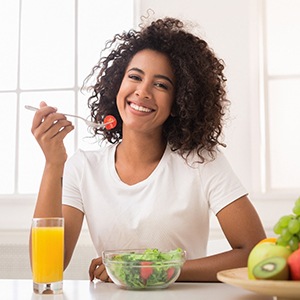 A young woman wearing a white shirt and eating a salad without her clear aligners